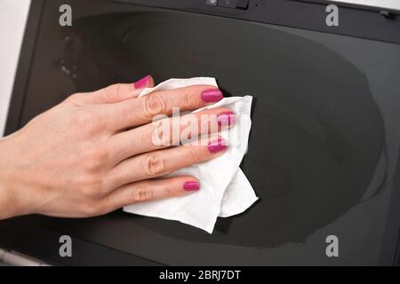 Woman cleaning laptop screen with white tissue, detail on her fingers holding paper towel Stock Photo