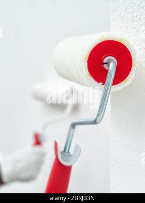 Caucasian house painter worker in white work overalls and with protective gloves, painting the wall with white paint using the roller. Construction in Stock Photo