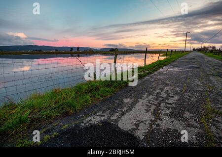 A flooded field along a country road at sunset. Stock Photo