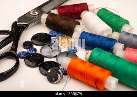 Several reels of multicolored sewing thread, multicolored buttons of different sizes, and large vintage sartorial scissors on a white background. Clos Stock Photo