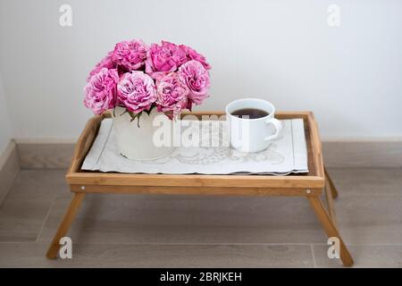 Bouquet of pink roses in a white tin bucket with the white cup of coffee on a wooden tray. Copy space Stock Photo