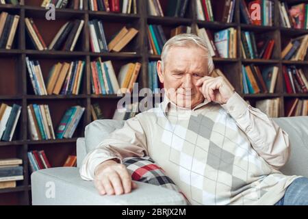 Senior man alone sitting at library crying unhappy remembering past days Stock Photo