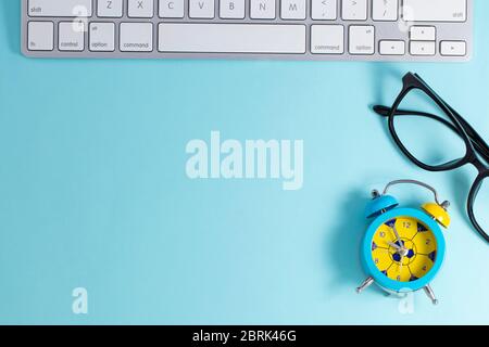 keyboard, glasses with with alarm clock on blue background, top view copy space. Business concept. Stock Photo