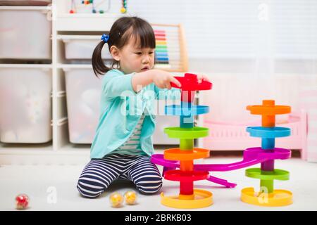 toddler girl play marble run game at home against white background Stock Photo