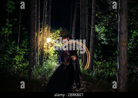 Young man in halloween cosplay holding a magic staff and swinging a magic pendulum in circles Stock Photo