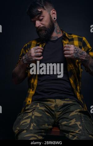 Bearded man with tattoos on his hands and neck wearing yellow black shirt and army pants Stock Photo