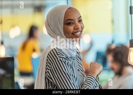 Protrait of a black ( african-american) female muslim standing in a modern business office while wearing a hijab. Stock Photo