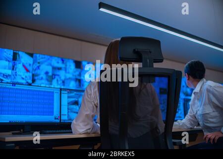 Group of Security data center operators (administrators) working in a group at a CCTV monitoring room while looking at multiple monitors ( computer sc Stock Photo