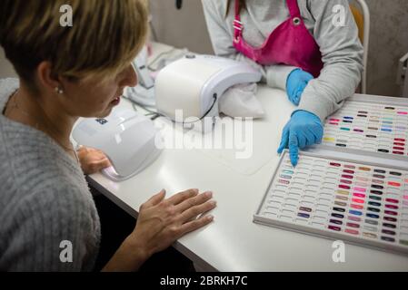 Concept: personal care, manicure. Manicurist working. young girl doing nail work on adult woman hands. Choosing from acrylic paint. Color chart. Palet Stock Photo