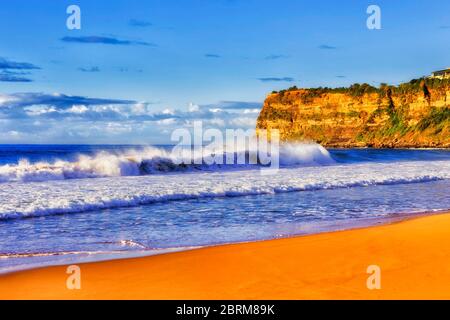 Clean strip of yellow sand on Sydney Northern beaches in warm soft morning light around Mona Vale head attacked by Pacific ocen waves. Stock Photo