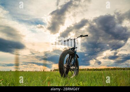 A Bicycle with thick wheels on a green meadow against a beautiful sky. Fatbike. Stock Photo