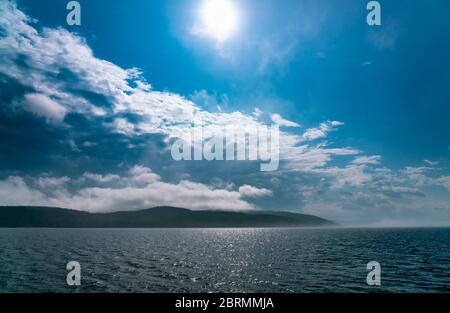 Sea fog laying over the sea disappears under strong morning sun, almost no wind, blue skies Stock Photo