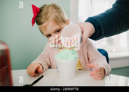 Mom pouring sprinkles on girls ice cream Stock Photo