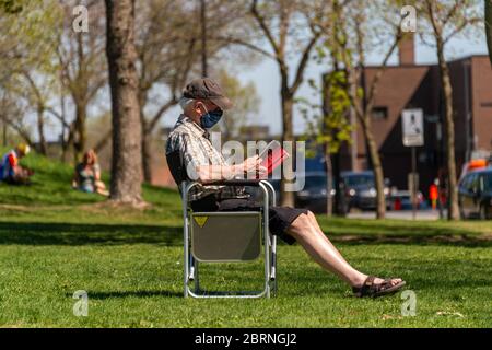Montreal, CA - 20 May 2020: Senior man with a face mask reading a book in Pelican Park  during Covid 19 pandemic Stock Photo