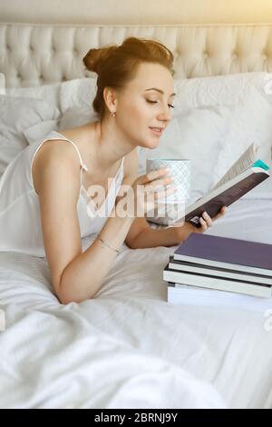 Happy young woomen relaxing on bed and reading book staying at home. Girl learning at home reading literature during quarantine Stock Photo