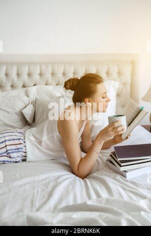 Happy young woomen relaxing on bed and reading book staying at home. Girl learning at home reading literature during quarantine Stock Photo