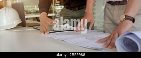 Cropped shot of two engineers working together with mock-up tablet and paperwork on white table in meeting room Stock Photo