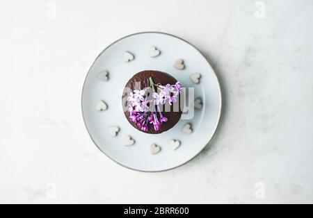 chocolate brownies cookies with lilac flower on a white porcelain saucer with wooden little hearts on marble white background Stock Photo