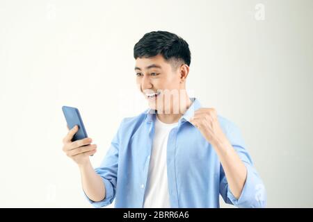 Image of excited happy young man posing isolated using mobile phone. Stock Photo