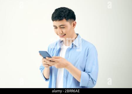 Relaxed young casual man reading text message on mobile phone isolated over white studio background. Stock Photo