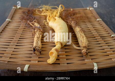 Fresh and dry ginseng on bamboo weave with the wood background. Stock Photo