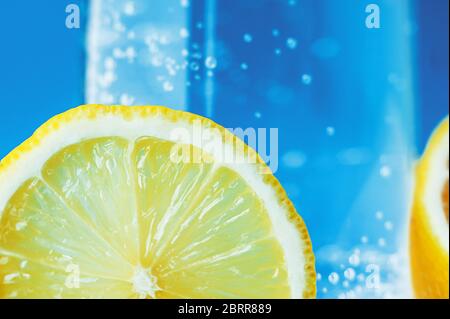 slice of ripe yellow fresh lemon close-up on a background of sparkling water with bubbles in a transparent glass. Vitamin C and Citrus for Health Stock Photo
