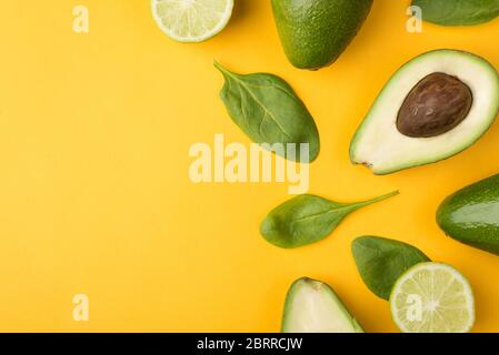Top above overhead view cropped photo of cut avocado, lemons and baby spinach leaves places to the right side isolated on yellow background Stock Photo