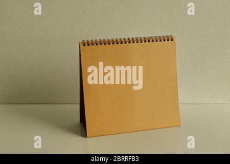Empty golden spiral binding desk calendar placed on white wooden table with sunlight and shadow Stock Photo