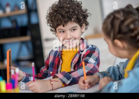 Curly boy and dark-haired girl sitting at table, doing their assignments, discussing something, smiling Stock Photo