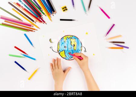 A child draws planet earth with felt-tip pens on white paper. Stay home. Stock Photo