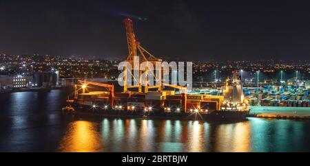 Night shot. Long exposure. Bridgetown port with loading crane and cargo ship being loaded with containers. Beautiful lights. Stock Photo