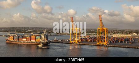 Bridgetown port with loading cranes and full cargo ship sailing away Stock Photo