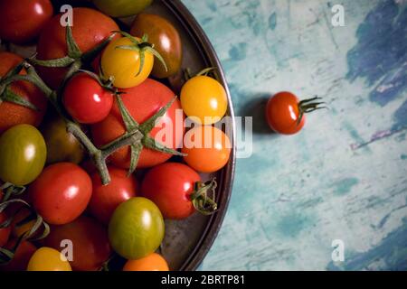 Colourful tomatoes on a pewter plate over old, painted wood background Stock Photo