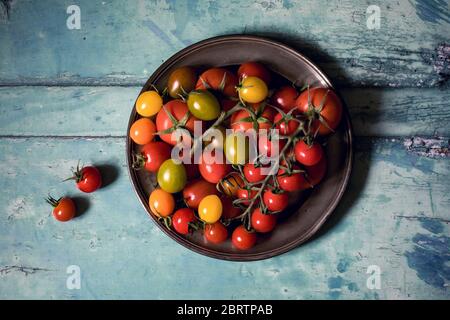 Colourful tomatoes on a pewter plate over old, painted wood background Stock Photo