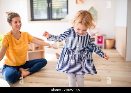 Cheerful young mother with small daughter indoors in bedroom playing. Stock Photo