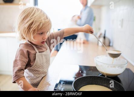 A small boy helping indoors in kitchen with making pancakes. Stock Photo