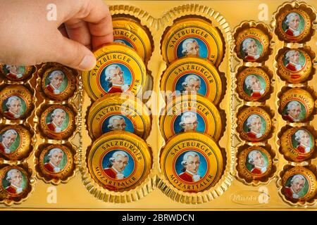 Tambov, Russian Federation - April 30, 2020 Woman hand taking candy from box filled of Mozartkugeln and Mozarttaler chocolates. Stock Photo
