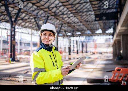 A woman engineer with tablet standing on construction site, working. Stock Photo