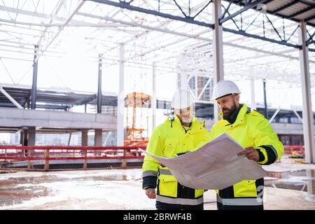 Men engineers standing outdoors on construction site, holding blueprints. Stock Photo