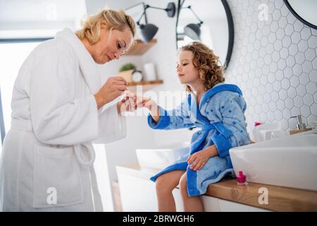 A cute small girl with mother in bathroom indoors at home, painting nails. Stock Photo