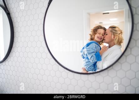 A reflection of mother and small daughter in mirror in bathroom.