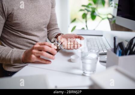 A businessman at the desk indoors in office, taking medicine pills, midsection. Stock Photo