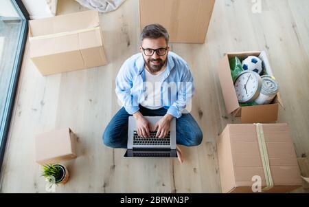 Top view of mature man with boxes moving in new house, using laptop. Stock Photo