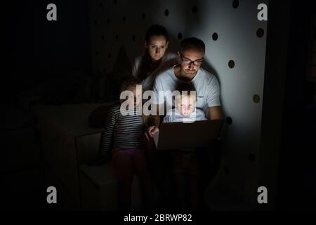 Family with children sitting indoors in bedroom, using laptop. Stock Photo