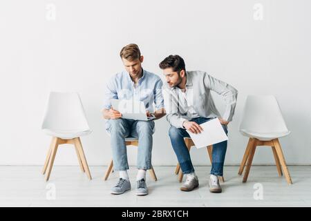 Two men with resume and laptop waiting for job interview on chairs in office Stock Photo