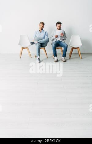 Handsome employees with resume and laptop sitting on chairs in office Stock Photo