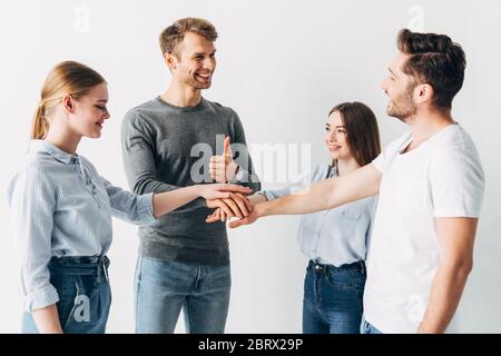 Smiling man showing thumb up while holding hands with coworkers in office Stock Photo