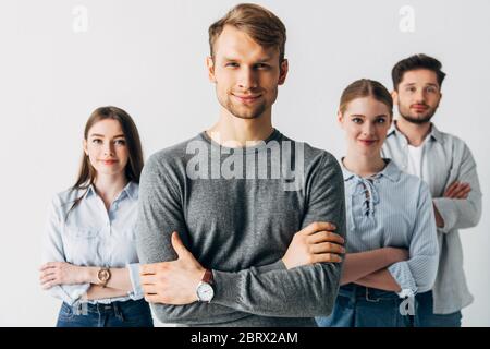 Selective focus of man smiling at camera near coworkers with crossed arms in office Stock Photo