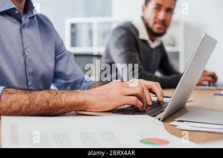Selective focus of businessman using laptop near african american colleague in office Stock Photo