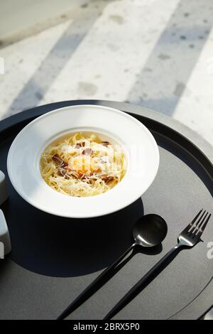 delicious pasta carbonara served with cutlery on black table on marble background in sunlight Stock Photo